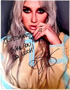 Autographed photo of a woman with long, wavy hair, wearing a yellow and blue hoodie. The message says, "DRIVESAVERS! THANK YOU SO MUCH!" followed by a signature.