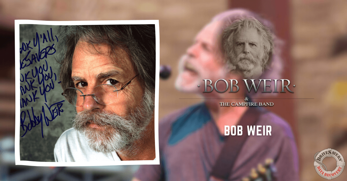 The image captures a close-up of a man with a bushy gray beard and glasses, likely Bob Weir. He is positioned against a blurred stage background, adding to the ambiance of the setting. The photo appears to be signed with a handwritten message on the left side.