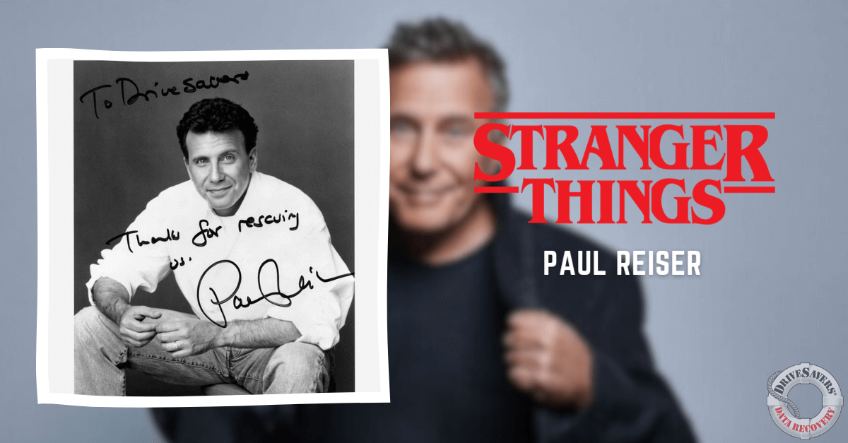 The image is a black and white photograph featuring a smiling Paul Reiser sitting casually. Handwritten messages on the photo include "To Diehard" and "Thanks for rescuing us, Paul Reiser." In the background, there is a blurred version of the same photo with references to "Stranger Things" and Paul's name. This suggests that Paul Reiser had a role related to these references in his career.