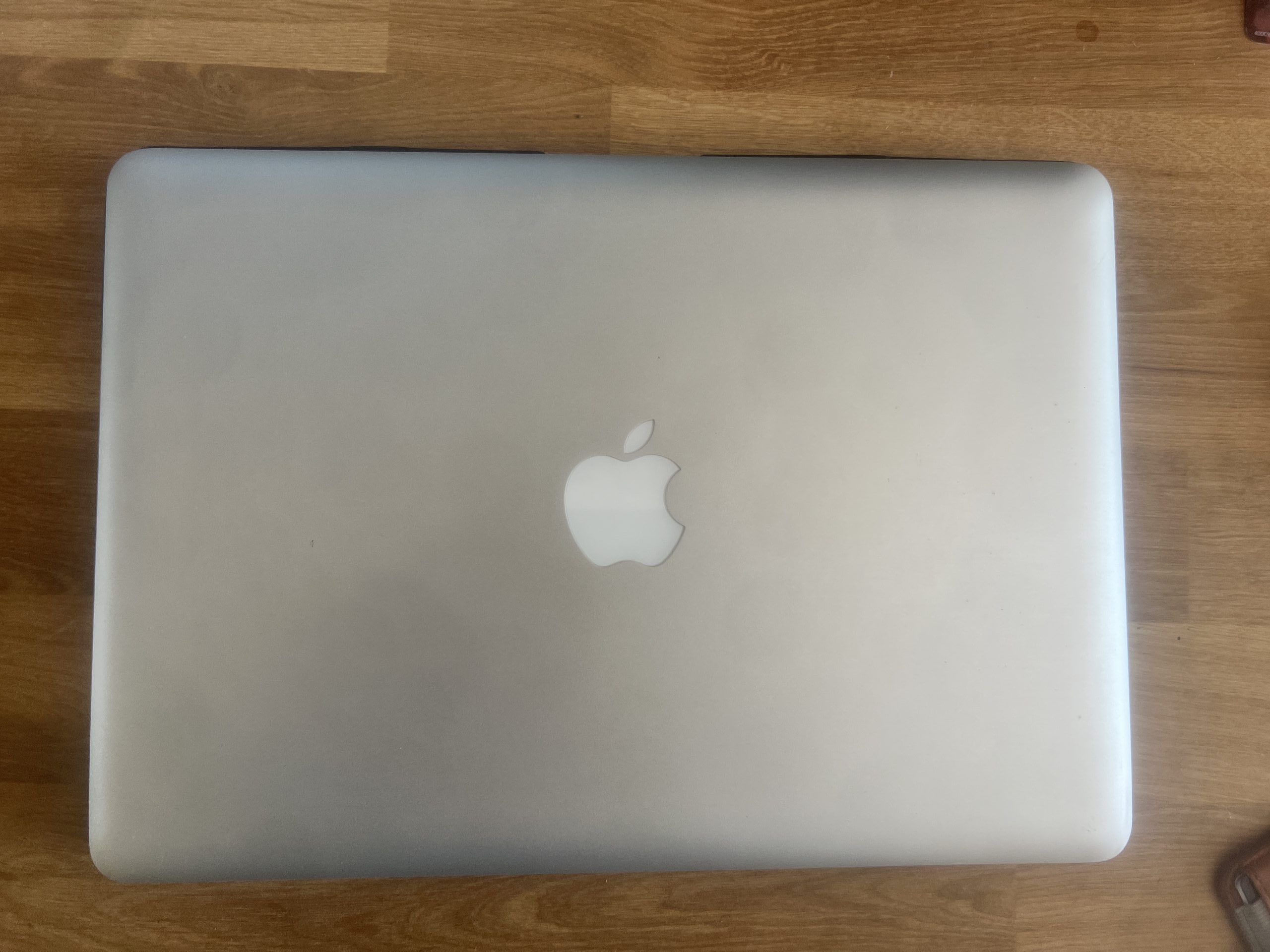 A closed silver laptop with an apple logo on the lid, placed on a wooden surface.