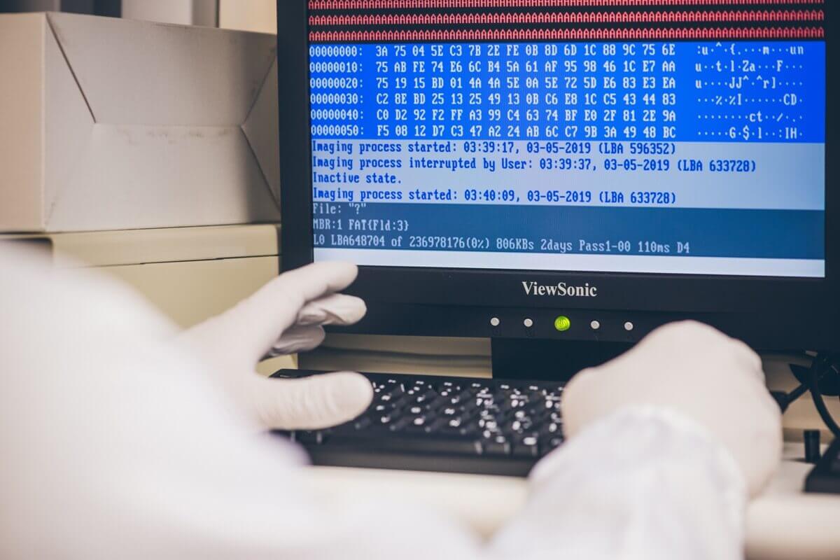 A person in white gloves is using a computer. The screen displays hexadecimal code and messages about an imaging process, including details such as dates, times, and statuses like "inactive state." A ViewSonic monitor is shown.